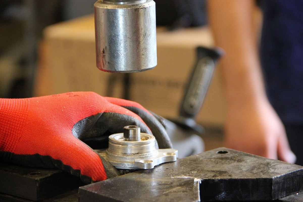Hand im Arbeitshandschuh richtet ein Lagerteil unter dem Stempel einer Presse aus